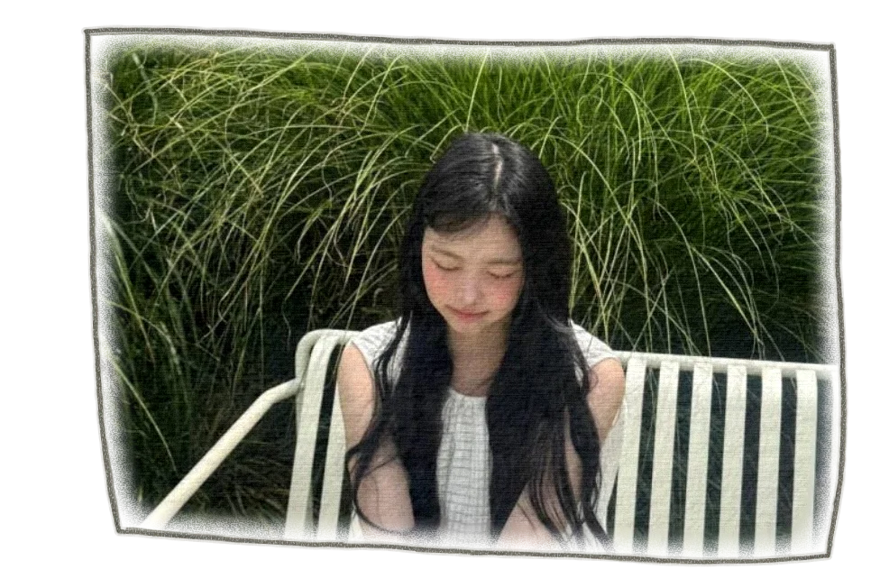 Ian in a white dress, sitting on a garden bench in front of tall green grasses